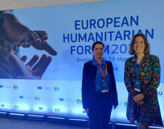 Photo of Gyöngyi Kovács (Hanken) and Claire Barnhoorn (Solvoz) at the European Humanitarian Forum 2024 in front of a forum poster.